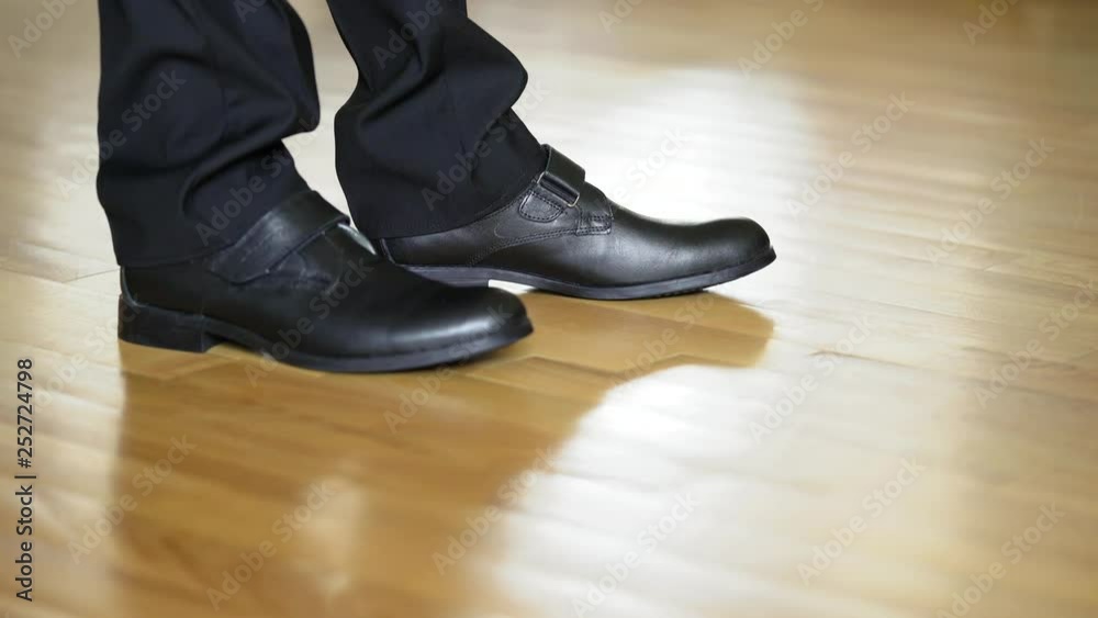 Man's legs shows black shoes standing on heels and goes away on the wooden floor. Legs of a young man in the dancing shoes. Close-up Man's legs shows black shoes standing on heels and goes away on the wooden floor. Legs of a young man in the dancing shoes. Close-up