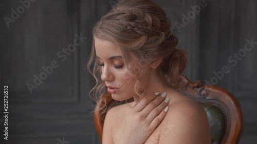 sweet beautiful lady with blond fair hair in spacious dark studio on expensive chair, advertisement for beauty salon, gentle look for prom 2019, professional work of makeup artist and hairdresser