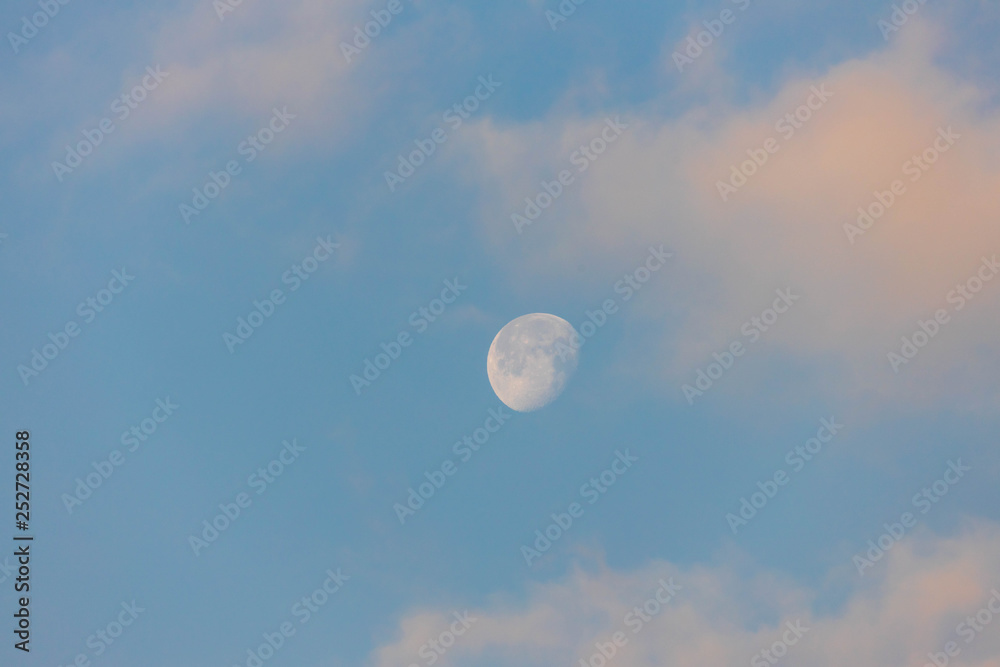 Three quarter moon against blue sky with pink clouds after sunrise Three quarter moon against blue sky with pink clouds after sunrise