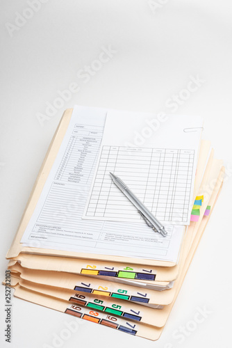 A stack of medical records in folders with color-coded and numbered tabs along with doctor's notes office visit form, ledger card and a pen.
