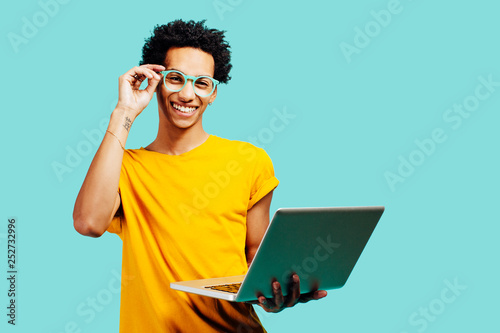 Portrait of a young man holding his laptop, isolated on blue background