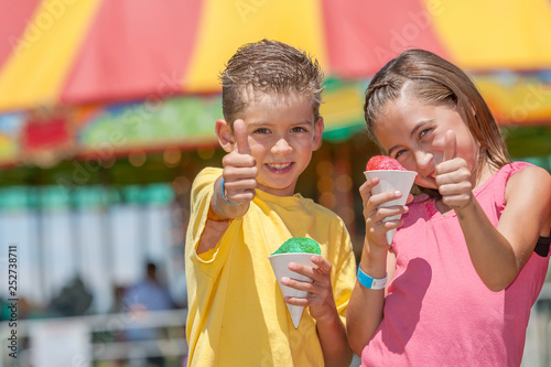 Two young kids eating snow cones at an amusement park, carnival or county fair.