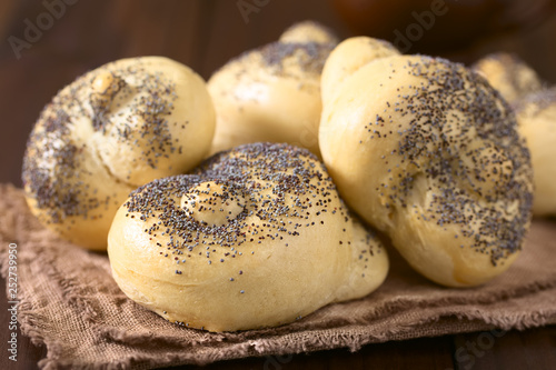 Homemade poppy seed bread rolls on fabric on dark wood, photographed with natural light (Selective Focus, Focus one third into the first roll)