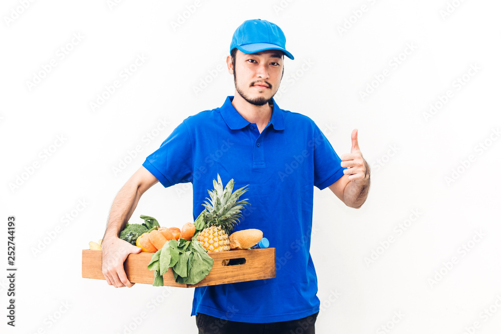 Happy delivery man in blue uniform carrying package of grocery food with vegetable and fruit on white background Happy delivery man in blue uniform carrying package of grocery food with vegetable and fruit on white background