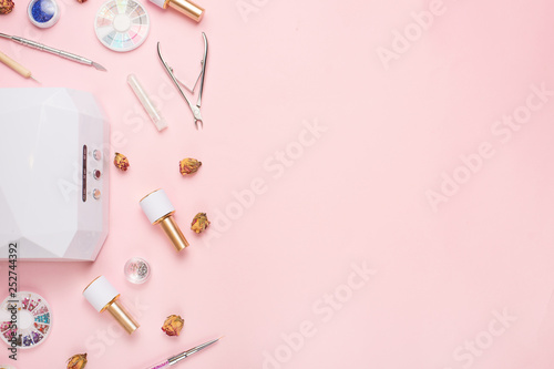 Beauty accessories for manicure and pedicure on a pink background,. Samples of nail polish, scissors, manicure ultraviolet machine, nippers and other accessories for home and salon procedures © Anton