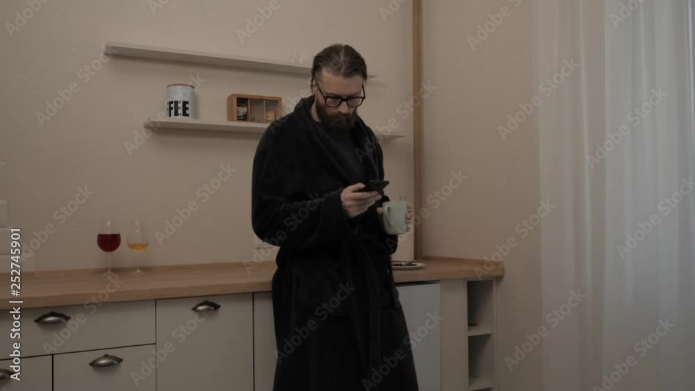 Bearded man with smartphone and cup of tea at kitchen, slow motion Bearded man with smartphone and cup of tea at kitchen, slow motion