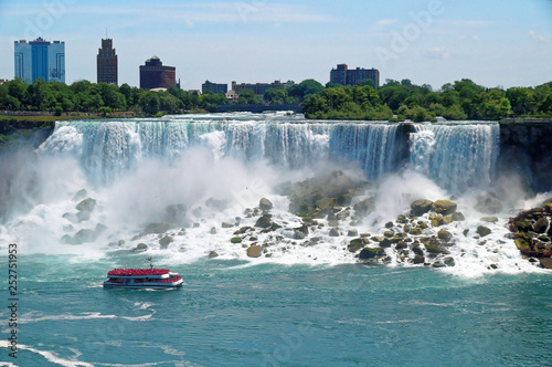 American Niagara Falls waterfall view with a touristic boat in front. The falls height is 57 m and they throw down about 6,400 m3 water per second