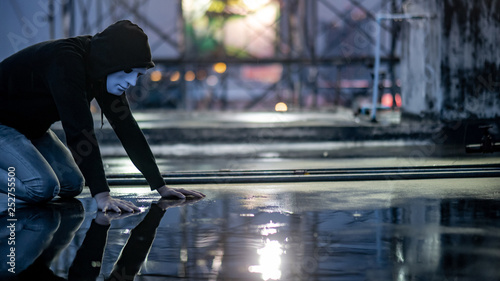 Reflection of mystery hoodie man in white mask feeling guilty looking his face on wet floor while raining. Sadness, depression and surrender concepts