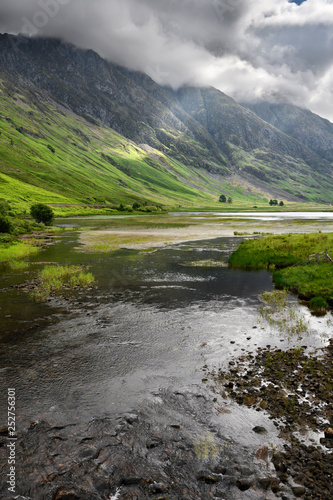 Loch Achtriochtan on the River Coe with dappled sun on the steep Aonach Eagach Ridge mountains in clouds Glen Coe Valley Scotland photo