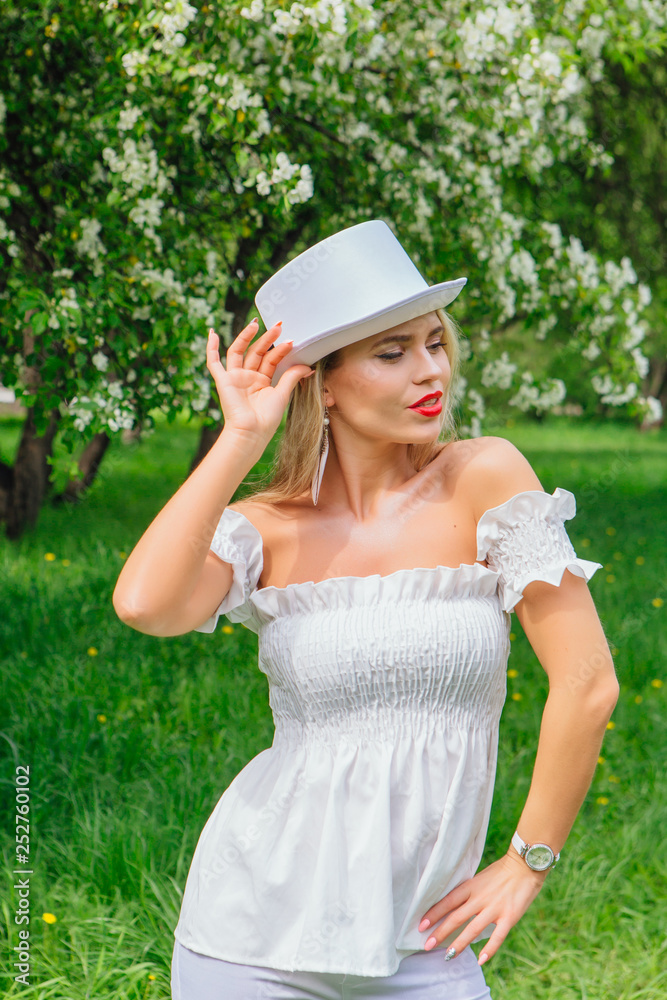 Sexy modern bride in white cylinder hat enjoing bloomin apple tree flowers.