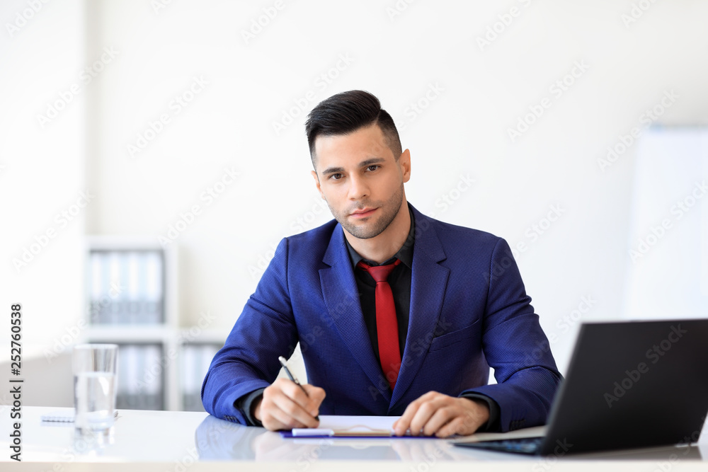 Young confident businessman signing document in the office