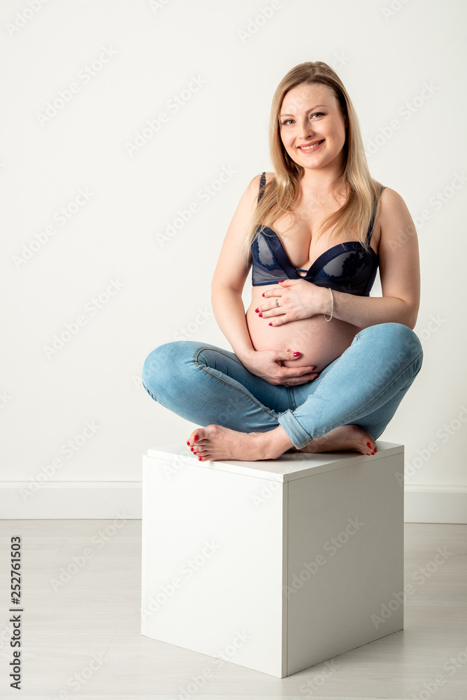 Beautiful pregnant woman blonde in blue jeans hugs belly on white background Beautiful pregnant woman blonde in blue jeans hugs belly on white background