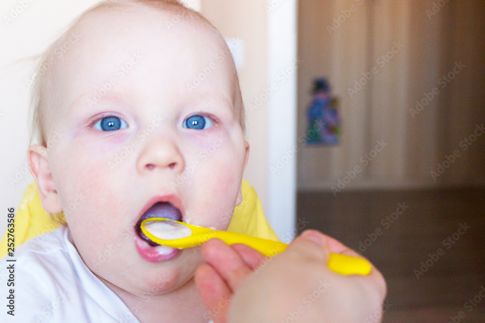 Mother feeds her little son porridge from a yellow spoon Mother feeds her little son porridge from a yellow spoon