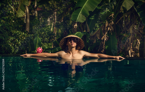 The guy in the infinity pool. Pool in the jungle. Holidays in Bali. The guy is tanning. Relax. Conical Asian hat.