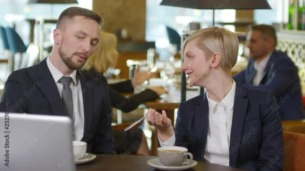 Medium shot of businessman and businesswoman sitting in café, looking at laptop screen, talking and laughing Medium shot of businessman and businesswoman sitting in café, looking at laptop screen, talking and laughing