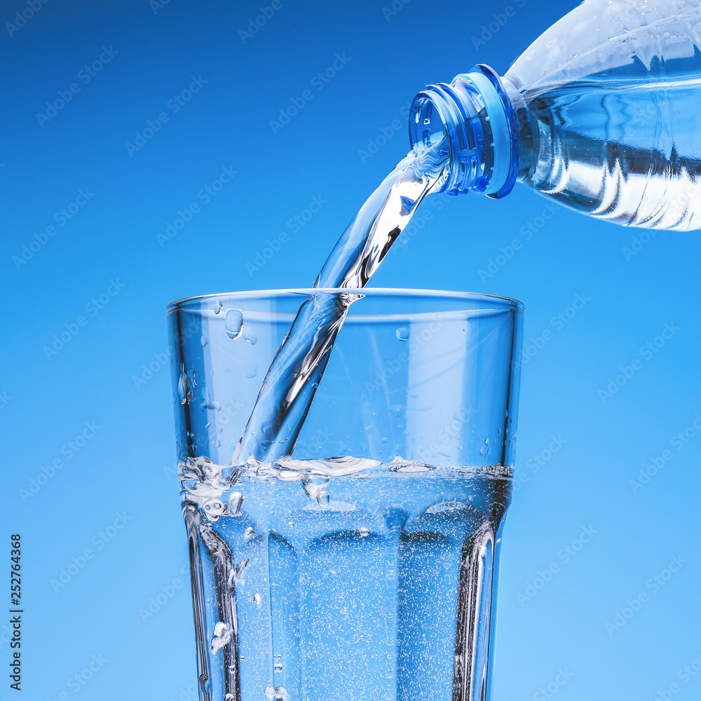 Pouring drinking water from plastic bottle into glass, against blue sky