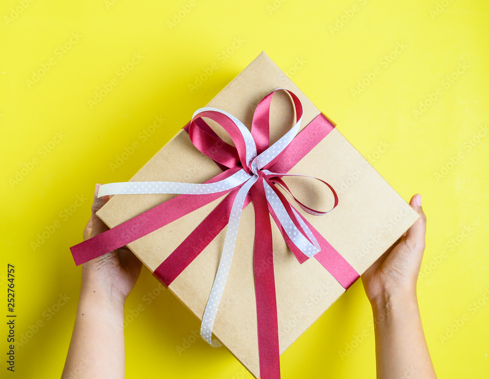 Hand holding gift box with bow on yellow background Hand holding gift box with bow on yellow background