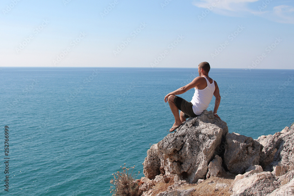 a man on a rock looking into the distance against the sea