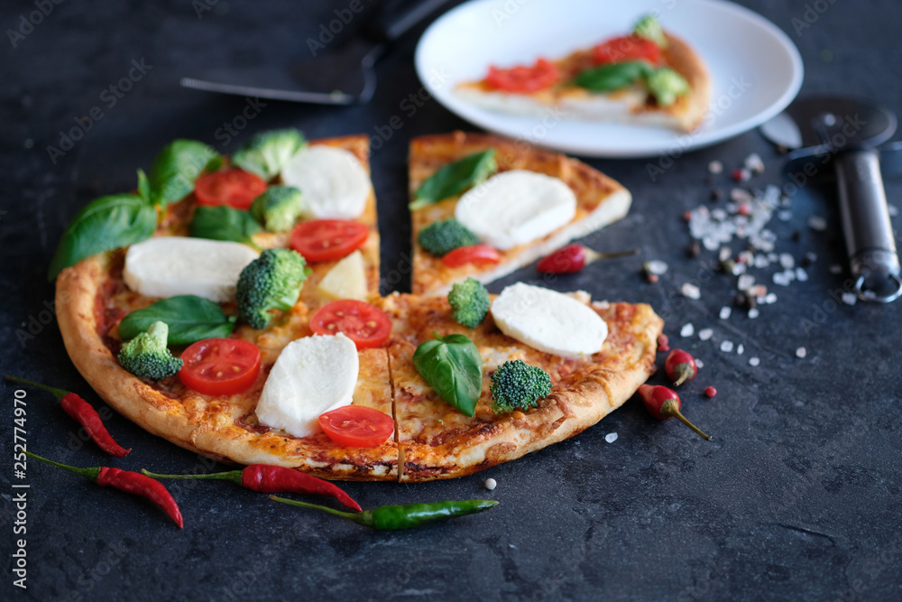Sliced pizza with Mozzarella cheese, tomatoes, broccoli, Spices and fresh basil on black stone background. Italian pizza. One peece of pizza on a plate Sliced pizza with Mozzarella cheese, tomatoes, broccoli, Spices and fresh basil on black stone background. Italian pizza. One peece of pizza on a plate