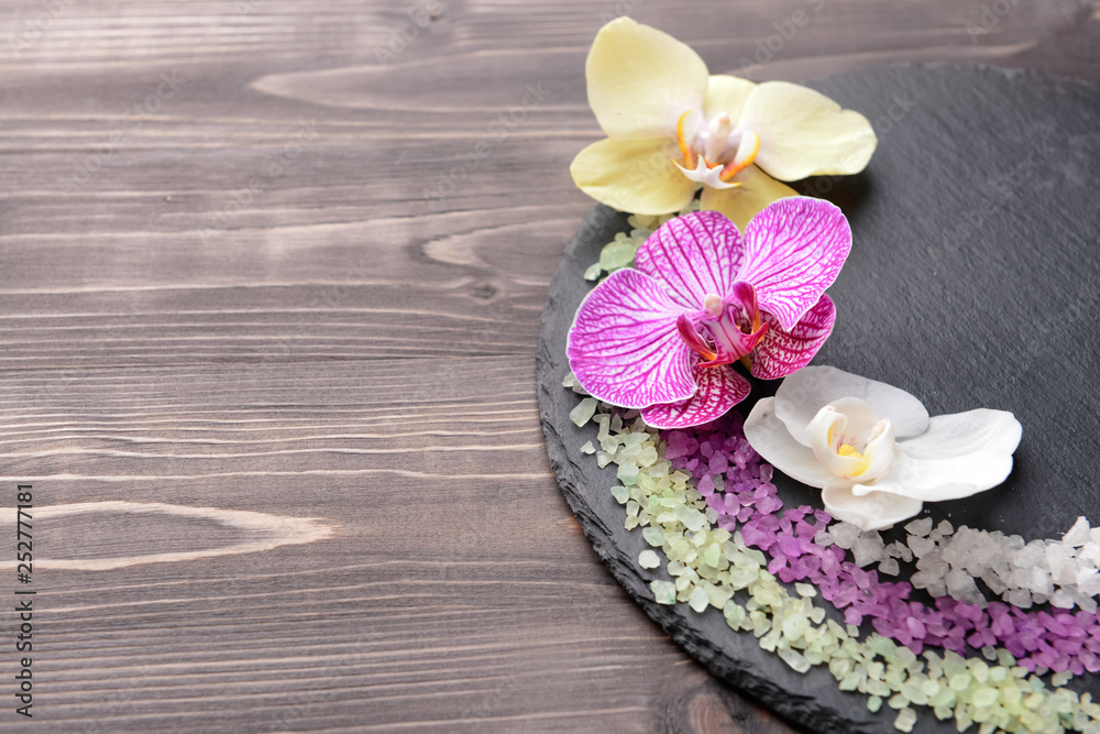 Slate plate with beautiful orchid flowers and sea salt on wooden background Slate plate with beautiful orchid flowers and sea salt on wooden background