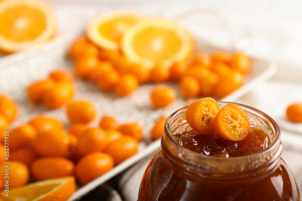 Jar with delicious kumquat jam on table, closeup