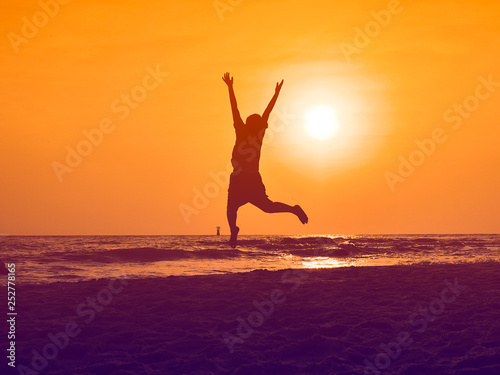 Silhouette boy jumping and raising hands on the beach in sun rise.