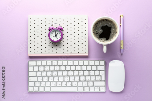 Computer keyboard, notebook, cup of coffee and alarm clock on color background photo