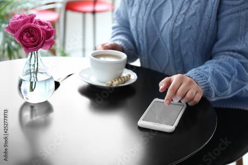 Young woman with mobile phone drinking coffee at table