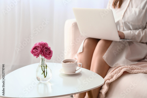 Young woman using laptop near table with cup of coffee at home