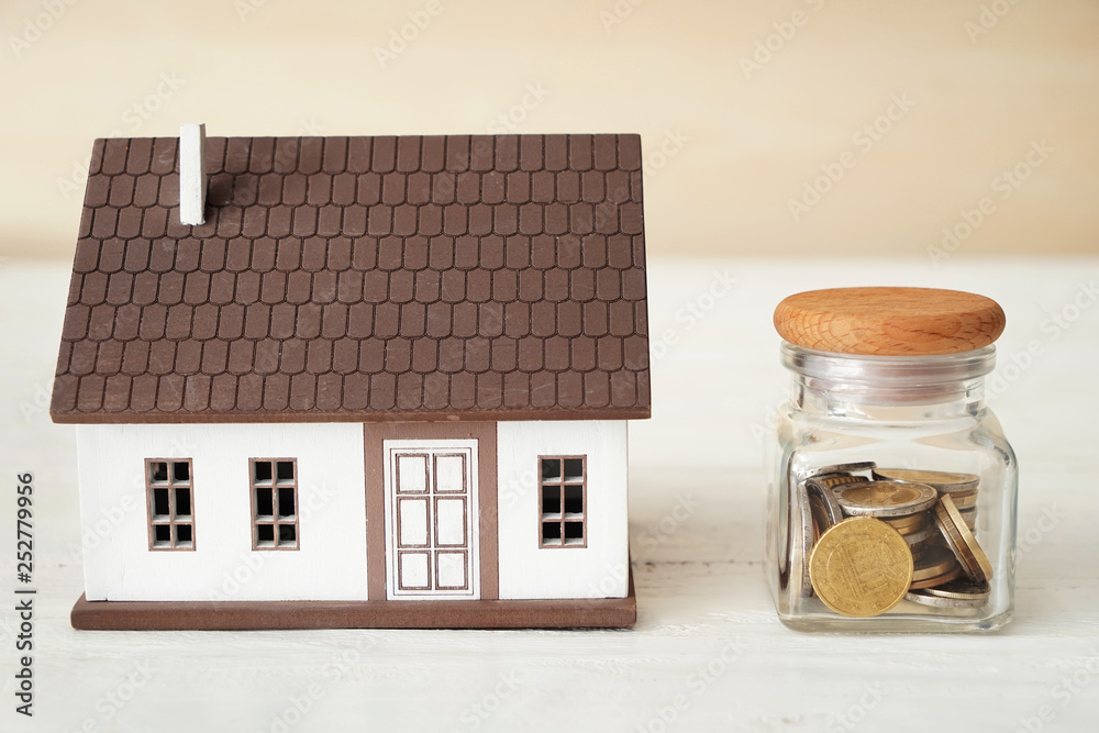 Jar with money and figure of house on table Jar with money and figure of house on table