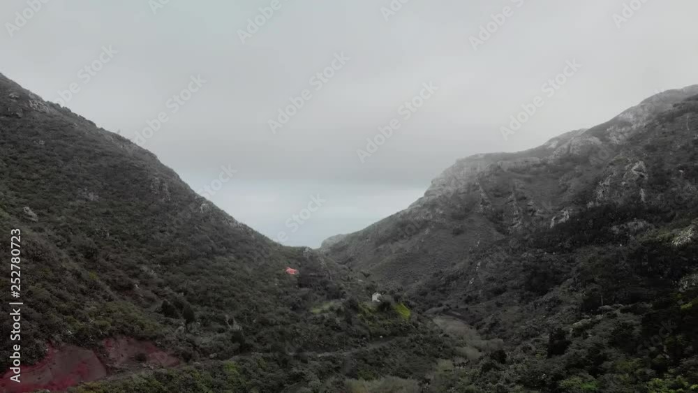 Aerial shot. Canyon between two hills. At the bottom of the canyon there are residential settlements and a village. Low storm clouds. Ocean ahead. Tenerife, Canary Islands. Dolly shot drone. Aerial shot. Canyon between two hills. At the bottom of the canyon there are residential settlements and a village. Low storm clouds. Ocean ahead. Tenerife, Canary Islands. Dolly shot drone.