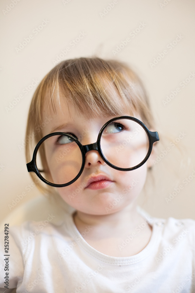 serious two years old girl in big black glasses on her nose closeup