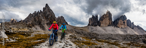 Cycling woman and man riding on bikes in Dolomites mountains andscape. Couple cycling MTB enduro trail track. Outdoor sport activity.