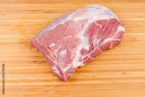Piece of uncooked pork neck on wooden cutting board