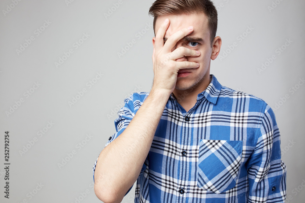 Scared guy dressed in a plaid shirt and jeans closes his face with his hand on a white background in the studio Scared guy dressed in a plaid shirt and jeans closes his face with his hand on a white background in the studio