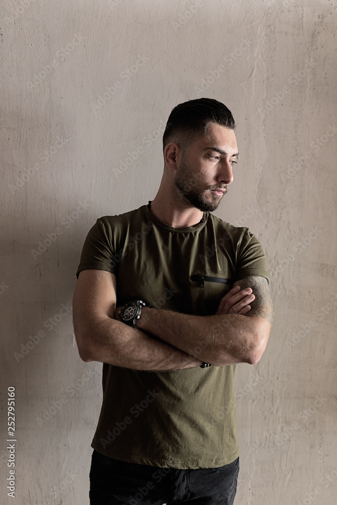 Handsome young man with a stylish hairstyle dressed in casual clothes stands on the wall background Handsome young man with a stylish hairstyle dressed in casual clothes stands on the wall background