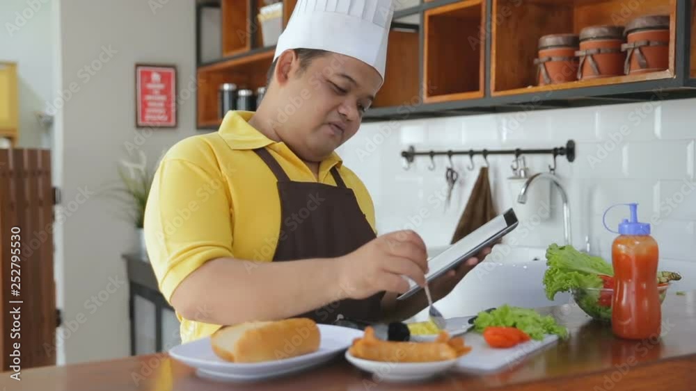 Young fat man preparing foods in the table and holding a tablet Young fat man preparing foods in the table and holding a tablet