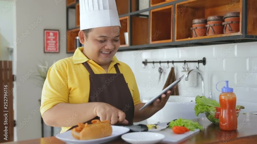 Young fat man preparing foods in the table and holding a tablet Young fat man preparing foods in the table and holding a tablet