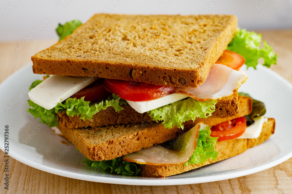 Healthy sandwich with greens, ham, tomatoes and cheese on wooden table Healthy sandwich with greens, ham, tomatoes and cheese on wooden table
