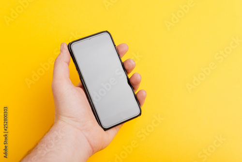 Handsome man hand holding a smartphone over yellow isolated background