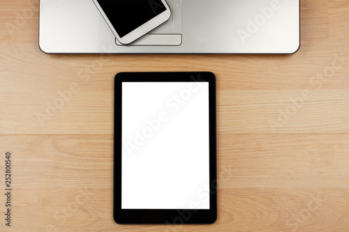 Digital tablet with blank screen and laptop with smartphone on wooden desk