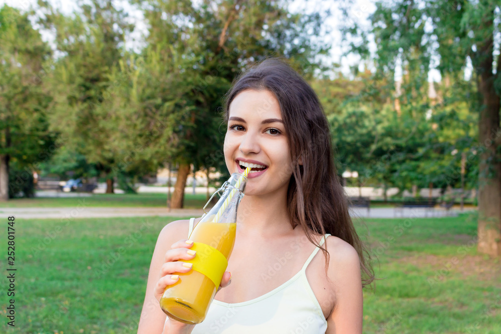 Attractive girl is drinking fresh juice through the straw outdoors. Pretty woman is holding a bottle of cold lemonade Attractive girl is drinking fresh juice through the straw outdoors. Pretty woman is holding a bottle of cold lemonade