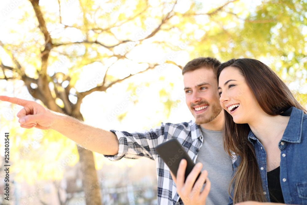 Fototapeta premium Happy couple holding phone pointing location in a park
