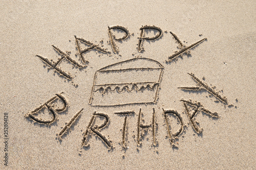 Photography Happy Birthday message handwritten in smooth sand with a slice of plain cake on