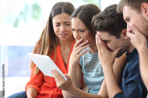 Worried friends checking tablet online news at home