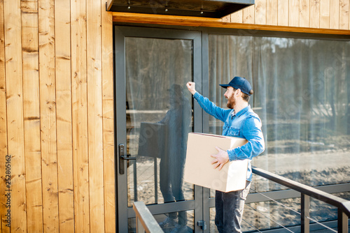 Delivery man knocking door of the modern house, delivering some goods in the paper parcel home