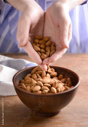 Woman pouring tasty almonds into bowl on table, closeup