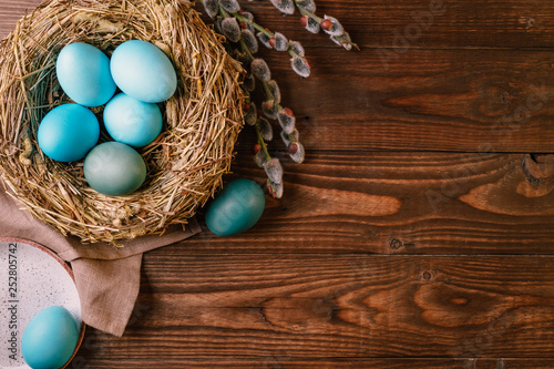 Turquoise colored Easter eggs in nest on vintage wooden background. Easter greeting card mock up with copy space, flat lay, above view.