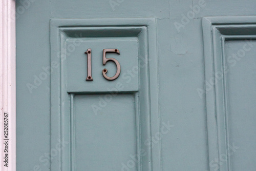 House number fifteen in silver numerals on a light green house door