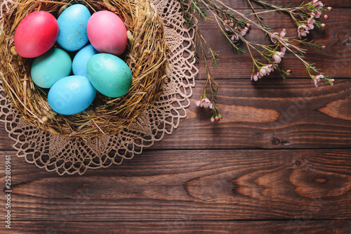 Dyed eggs in bird nest for Easter decoration and flowers on wooden desk.